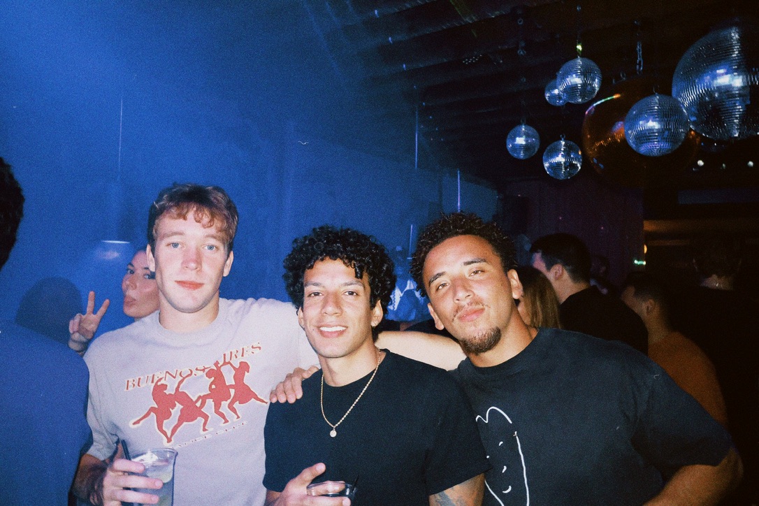 Three friends together beneath blue lights and disco balls