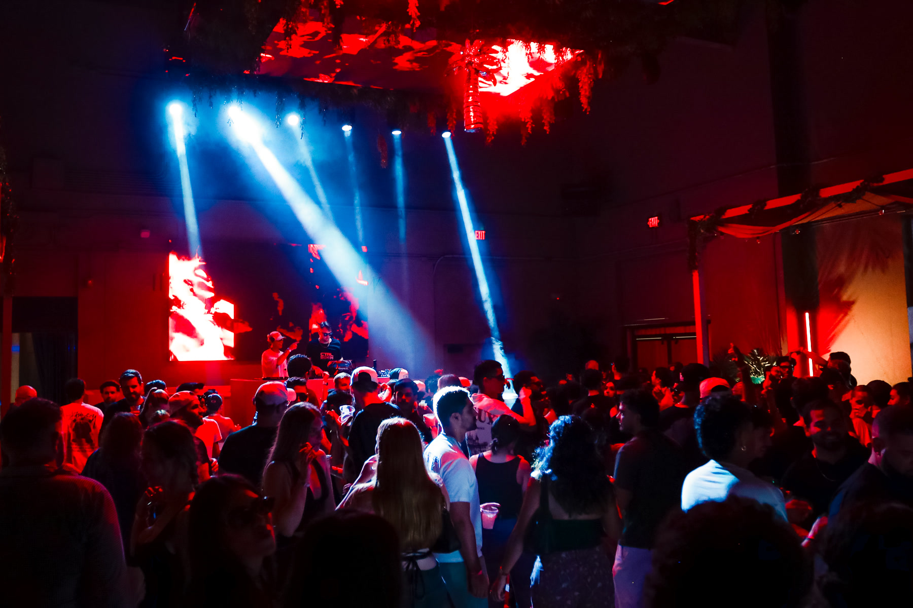 A full dance floor beneath blue spotlights and red stage visuals