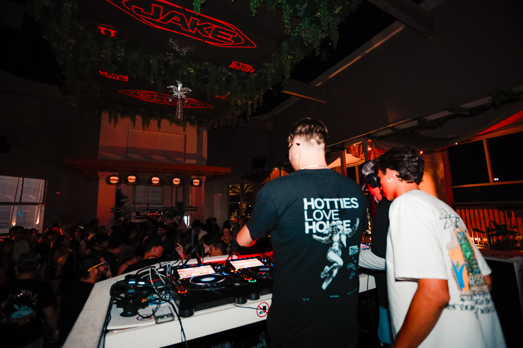 DJs at the booth overlooking the crowd beneath red ceiling visuals